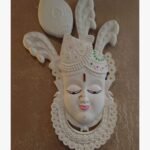 An original white wall sculpture titled 'Divine Grace', featuring an intricately detailed deity face with traditional motifs.