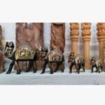 A set of four ornate, hand-painted wooden camel figurines from Rajasthan featuring traditional Indian folk art motifs on a display shelf.