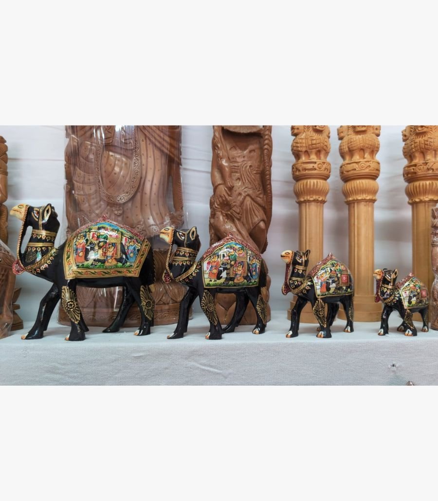 Royal Caravan Miniature Set by Rajasthan Artisan Collective A set of four ornate, hand-painted wooden camel figurines from Rajasthan featuring traditional Indian folk art motifs on a display shelf.