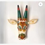 A handcrafted wooden bull head wall sculpture featuring vibrant traditional Indian folk art motifs and floral patterns on a cream background.