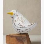A hand-carved white wooden songbird sculpture with a distressed finish perched on a natural rustic wood block base.