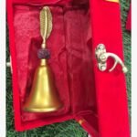 A premium handcrafted gold-finish brass ritual bell featuring a sacred Rudraksha bead and an intricate leaf-motif handle, presented in a luxury red velvet box.