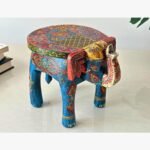 A vibrant, hand-painted wooden elephant stool featuring intricate traditional Indian floral patterns in blue, red, and gold, used as decorative accent furniture.