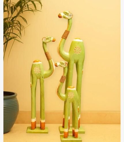 A set of three hand-carved wooden camel sculptures in varying sizes, painted in a soft matte green with jute neck accents and floral motifs.