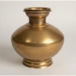 A premium handcrafted gold-finish brass ritual bell featuring a vertical feather-motif handle and a sacred Rudraksha bead, presented in a luxury red velvet box.