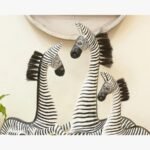 A set of three hand-carved wooden zebra sculptures featuring detailed black and white stripes and natural fiber manes, displayed in a gallery setting.
