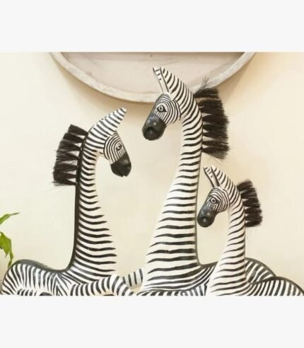 A set of three hand-carved wooden zebra sculptures featuring detailed black and white stripes and natural fiber manes, displayed in a gallery setting.