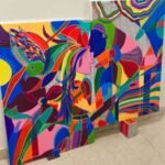 A large-scale vibrant abstract acrylic painting by Mansi Virani depicting a colorful, stylized embrace between two figures surrounded by a multi-colored bird and floral motifs.