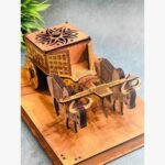 A perspective view of a handcrafted wooden bullock cart featuring intricate laser-cut sun motifs and golden metallic accents on a polished wooden base.