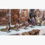 A set of hand-painted wooden peacock figurines with intricate blue paint and semi-precious stone inlay, titled Royal Peacock Procession.