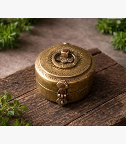A circular hand-engraved antique brass spice or jewelry box featuring intricate traditional patterns and a hinged clasp on a rustic wood surface.