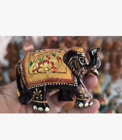 A miniature wooden elephant figurine intricately hand-painted with traditional gold, red, and black floral patterns, held in a palm.