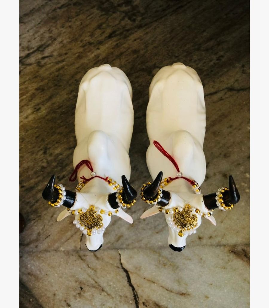 Sacred Adorned Nandi Bull Sculptures A top-down view of two white marble-finish Nandi bull sculptures adorned with traditional golden jewelry, pearls, and black horns.