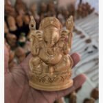 A finely detailed, hand-carved wooden sculpture of Lord Ganesha seated on a lotus throne, held in a palm.