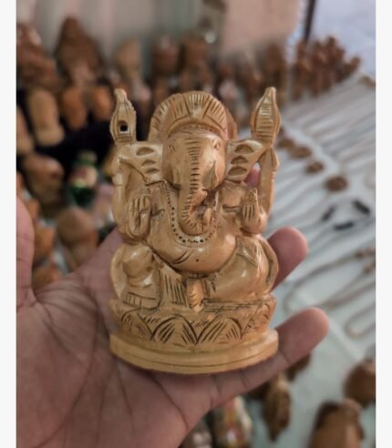 A finely detailed, hand-carved wooden sculpture of Lord Ganesha seated on a lotus throne, held in a palm.
