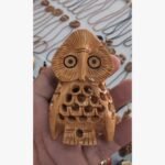 An intricately hand-carved wooden owl figurine with detailed plumage patterns and expressive eyes, held in a palm.