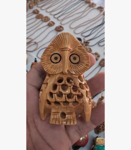An intricately hand-carved wooden owl figurine with detailed plumage patterns and expressive eyes, held in a palm.