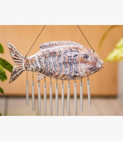 A hand-carved wooden fish wind chime with a distressed white and brown finish featuring hanging metallic chimes for coastal home decor.