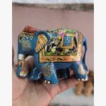 A miniature blue wooden elephant figurine featuring intricate hand-painted royal motifs and gold floral detailing, held in a palm.