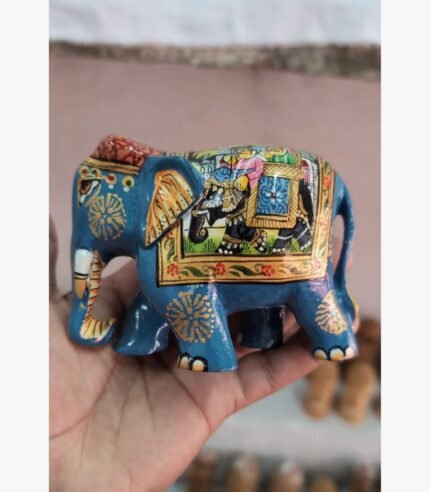 A miniature blue wooden elephant figurine featuring intricate hand-painted royal motifs and gold floral detailing, held in a palm.