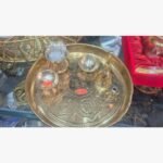A traditional 6-piece brass pooja thali set featuring an etched Swastika central motif, ritual bell, incense holder, and prayer bowls.