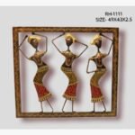 Handcrafted tribal women dancing metal wall art panel featuring three stylized figures with traditional headgear balanced inside a patterned square frame.