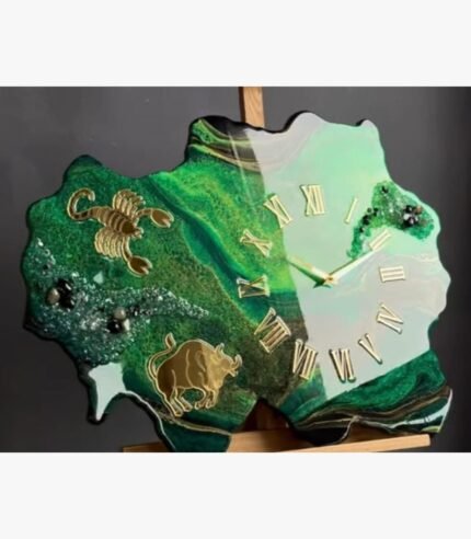 Luxury custom-shaped green geode epoxy resin wall clock titled Emerald Zodiac by Vina Bhavsar featuring gold Scorpio and Taurus astrological signs, golden Roman numerals, and textured emerald crushed crystal clusters.