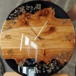 Handcrafted large circular wall clock titled Chronos by Vina Bhavsar combining live edge burl wood, black epoxy resin, gold Roman numerals, and metallic steampunk gears under a high-gloss finish.