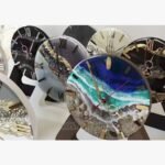 Handcrafted circular ocean wave epoxy resin clock titled Ocean Surge by Vina Bhavsar featuring realistic layered sea foam, deep blue water gradients, and a sandy beach shoreline with real seashells.