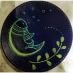 Handcrafted circular decorative plate titled Midnight Matsya by Vina Bhavsar featuring a minimalist stylized fish illustration in lime green and yellow outlines on a deep indigo blue background with bubbles and a botanical leaf vine.