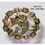 Handcrafted circular Lord Ganesha metal wall art panel featuring a textured iron Ganpati face holding a laddu modak and a green leaf within an ornate painted frame.