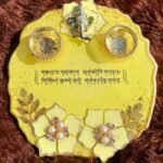 Handcrafted circular yellow epoxy resin pooja thali platter titled Vakratunda Mahakaaya by Vina Bhavsar featuring a silver Lord Ganesha idol, two matching diya bowls, Sanskrit shloka inscription, and pearl floral accents.