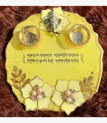 Handcrafted circular yellow epoxy resin pooja thali platter titled Vakratunda Mahakaaya by Vina Bhavsar featuring a silver Lord Ganesha idol, two matching diya bowls, Sanskrit shloka inscription, and pearl floral accents.