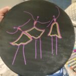 Handcrafted circular decorative plate titled Midnight Dancers by Vina Bhavsar featuring three minimalist stylized stick-figure ballerinas sketched in neon purple, pink, and lime green lines on a solid matte black background.