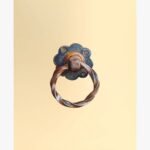Timeworn Reflections realistic acrylic painting by Harshita Siddhpura featuring an intricate antique rusted metal door knocker ring against a smooth cream color background.