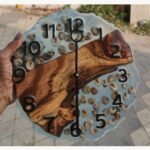 A premium scalloped-edge circular wall clock titled Ocean Echo by Vina Bhavsar combining a diagonal live edge wood slab, semi-translucent clear epoxy resin, real sea snail shells, and bold black numbers.