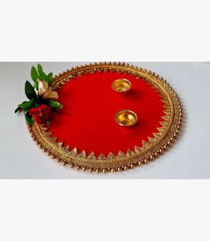 Handcrafted circular red decorative pooja thali platter titled Crimson Festive Elegance by Khushboo Gohel featuring ornate gold gota patti lace, golden bead trim, two brass diyas, and a faux rose accent.