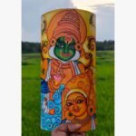 Hand-painted terracotta vase titled Divine Resonance by Akshaya Sivadas featuring a traditional Kerala mural portrait of a green-complexioned Lord Krishna playing a flute alongside Radha on a yellow ochre background.