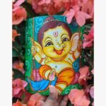 Hand-painted terracotta vase titled Bal Ganesha Swing by Akshaya Sivadas featuring a whimsical, traditional Kerala mural depiction of a joyful child Ganesha riding a swing on a vibrant green backdrop.