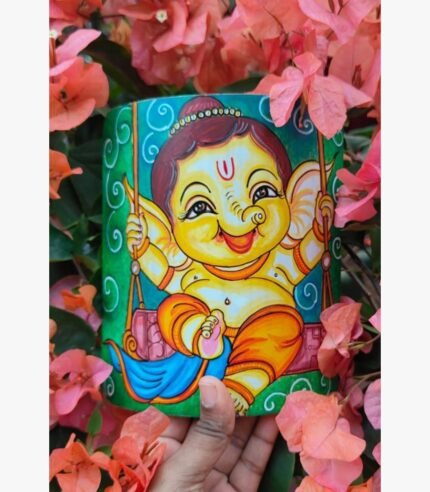 Hand-painted terracotta vase titled Bal Ganesha Swing by Akshaya Sivadas featuring a whimsical, traditional Kerala mural depiction of a joyful child Ganesha riding a swing on a vibrant green backdrop.
