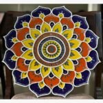 Handcrafted circular Lippan art wall hanging featuring royal purple, orange, and yellow scalloped lotus mandala patterns with mirror work by artist Rucha Desai.