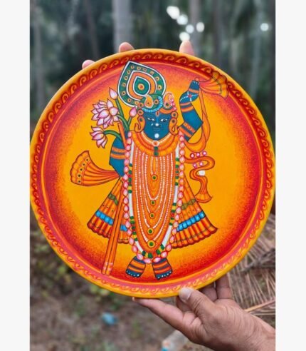 Hand-painted decorative terracotta plate titled Shrinathji Divine Radiance by Akshaya Sivadas featuring a full-body standing portrait of Lord Shrinathji with a peacock feather and lotus blossoms against a glowing orange and yellow backdrop.