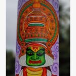 Hand-painted terracotta vase titled Kathakali Reverie by Akshaya Sivadas featuring a detailed green-faced Kathakali dancer with an elaborate golden crown on a lavender background.