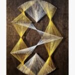 Modern abstract geometric string art on a dark textured wood board titled Kinetic Helix by Asit Trivedi featuring interwoven golden yellow and white threads forming complex diamond and hourglass tension patterns.