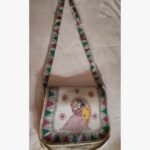 A hand-painted Madhubani folk art fabric sling bag featuring a traditional Indian woman motif and geometric borders by artist Bhavna Mishra.