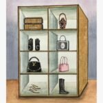 Original contemporary watercolor painting titled The Sartorial Vault by Hardev Chauhan showcasing a surreal wooden display cabinet filled with luxury fashion accessories, handbags, and shoes on a washed blue background.