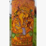 Hand-painted terracotta vase titled Mridangam Ganesha by Akshaya Sivadas featuring a detailed yellow Lord Ganesha playing a traditional drum on a golden ochre background.