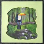 An original 3D paper cut-out and acrylic canvas painting of a colorful toucan perched in a tropical rainforest by artist Jyoti Machigad.