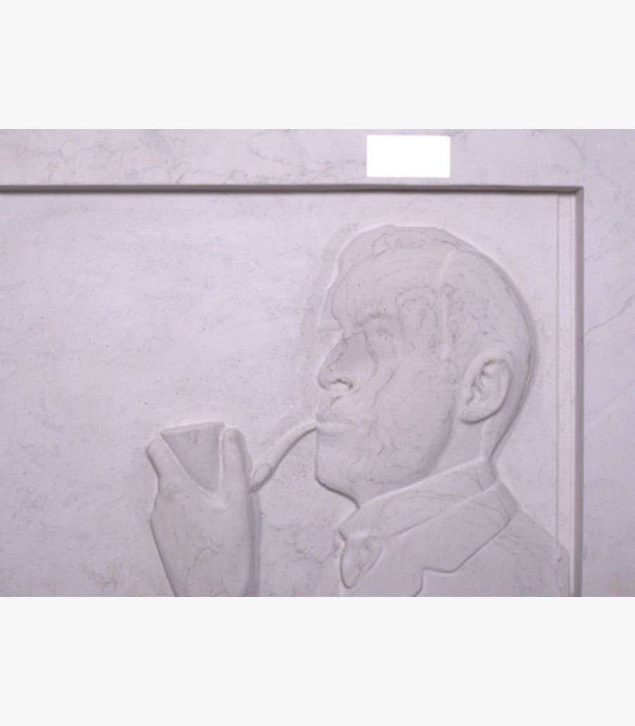 a Hand-carved white marble bas-relief sculpture titled The Pipe Smoker by Julian Vance depicting a side profile portrait of a man holding and smoking a classic tobacco pipe.