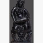 Hand-carved black stone sculpture titled Lady Playing Dholak by Mangalya Stone Panels showcasing a traditional Indian woman musician playing a drum in a classical dancing posture.